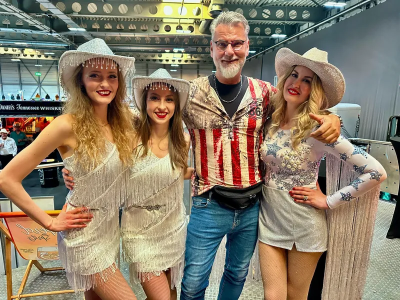 Messeteam in Westernkleidung vor der beleuchteten Truck-Bar