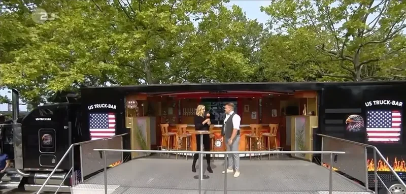 Die Truck-Bar mit US-Flagge und Barhockern im Grünen