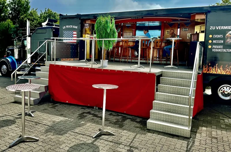 Die aufgebaute Bar mit Stehtischen, Treppe und Vermietungshinweis